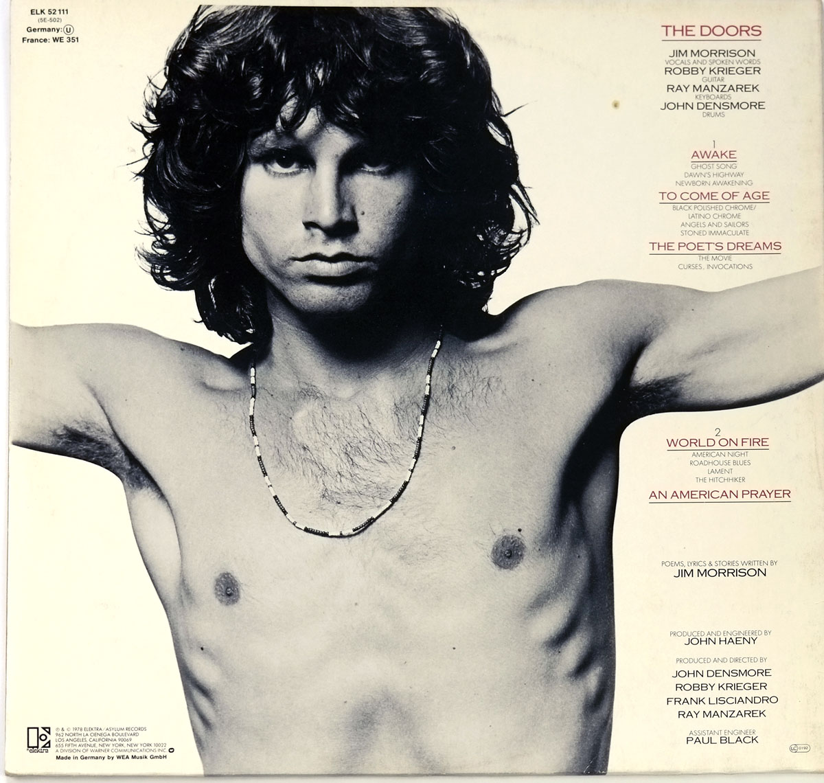 Back cover of An American Prayer by Jim Morrison and The Doors featuring a black-and-white photograph of a shirtless Jim Morrison with an intense gaze, alongside the tracklist and credits in red and black text, highlighting the album’s structure and production details.